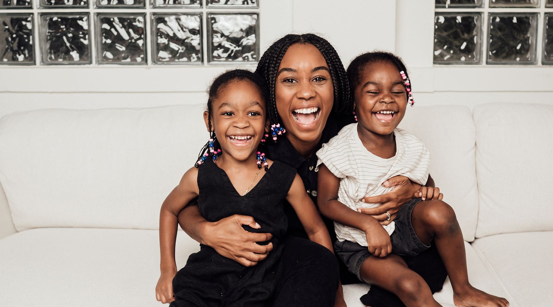 a mom and two young girls sitting on a couch and laughing