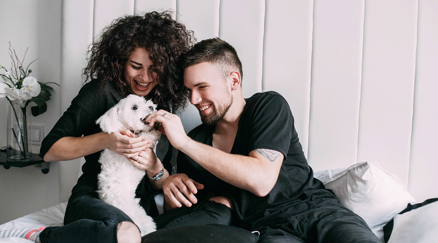 a man and a woman feeding a small dog and smiling